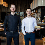 Two men wearing slim fit Men's Work Shirt in black and white, standing in a modern restaurant setting.