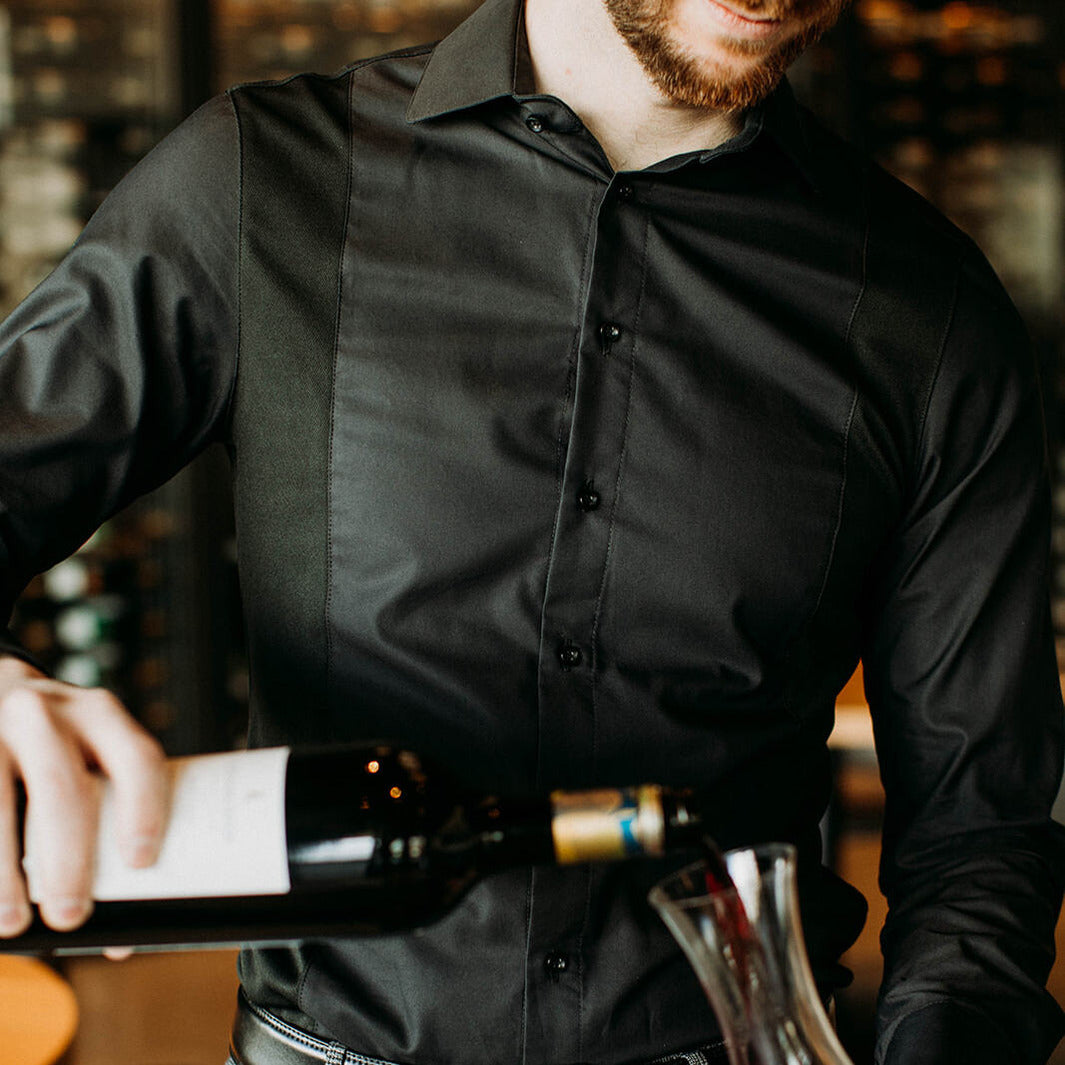 The front of a model wearing a black sweatproof work shirt for men pouring wine into a decanter