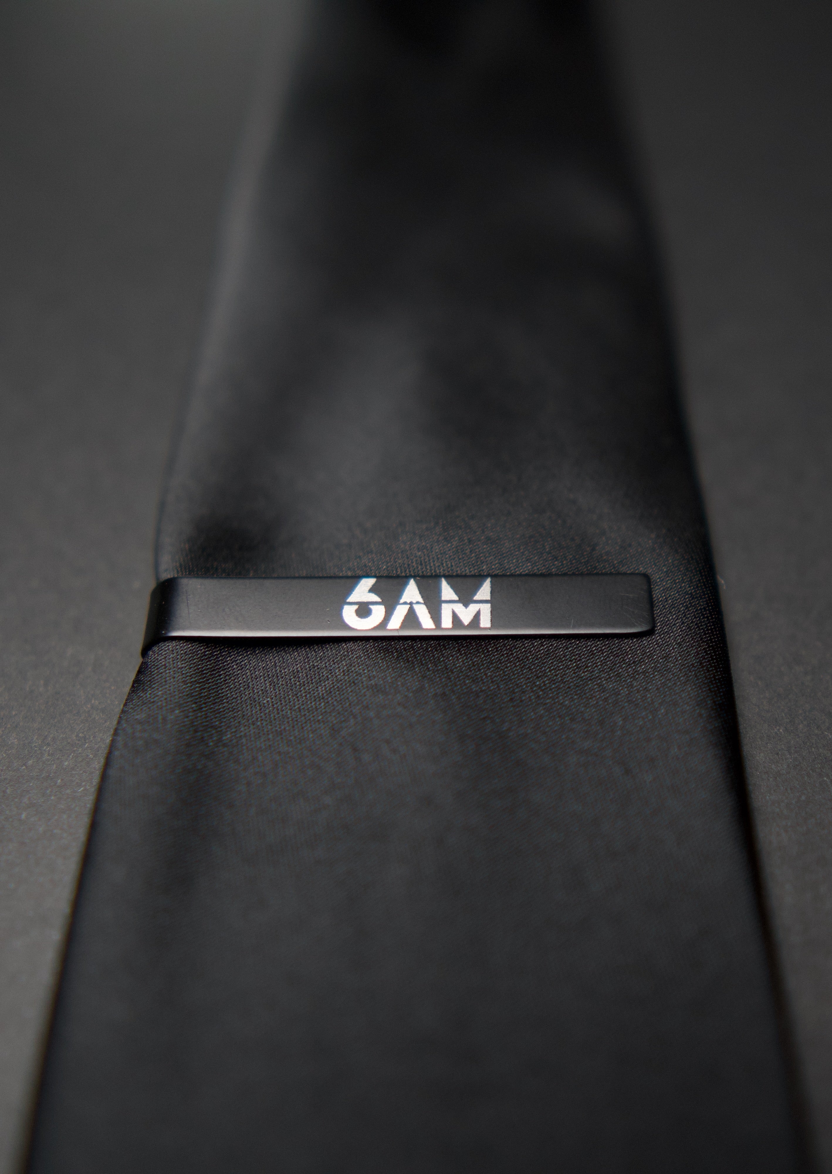 6AM Tie Clip handmade black stainless steel with 6AM logo engraved on a black tie close-up view