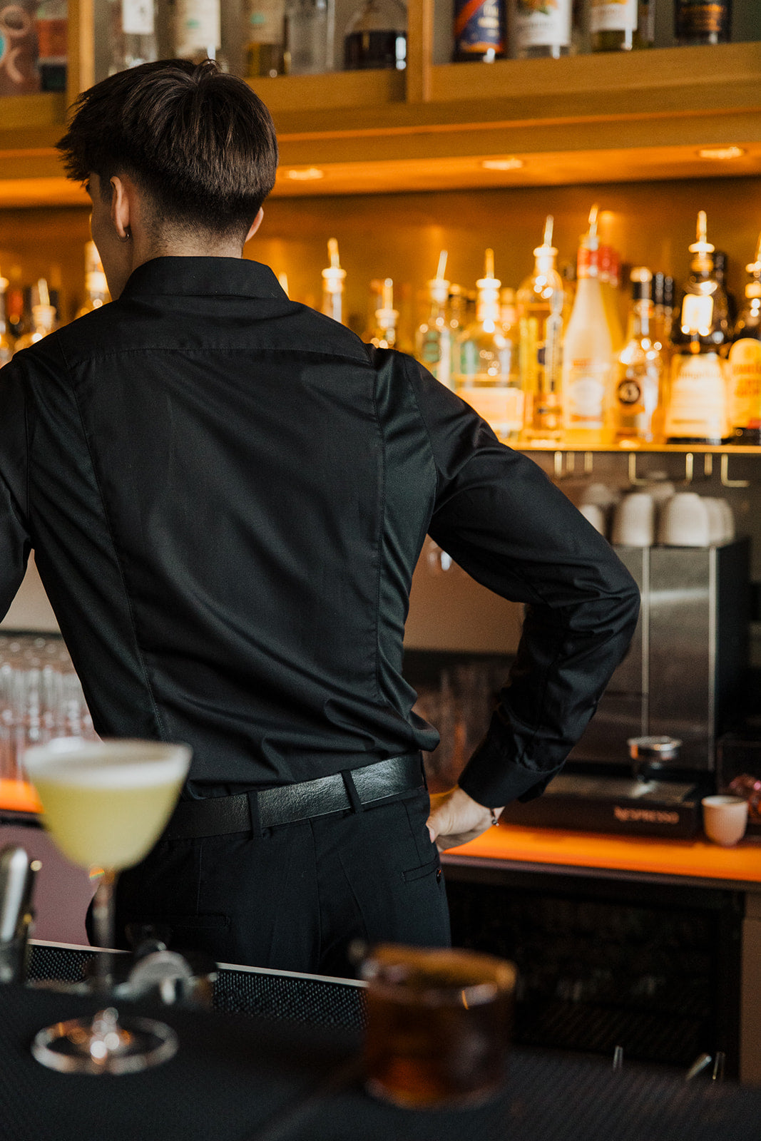 Men's Work Shirt slim fit sweat-proof design worn by bartender behind bar with drinks and bottles.