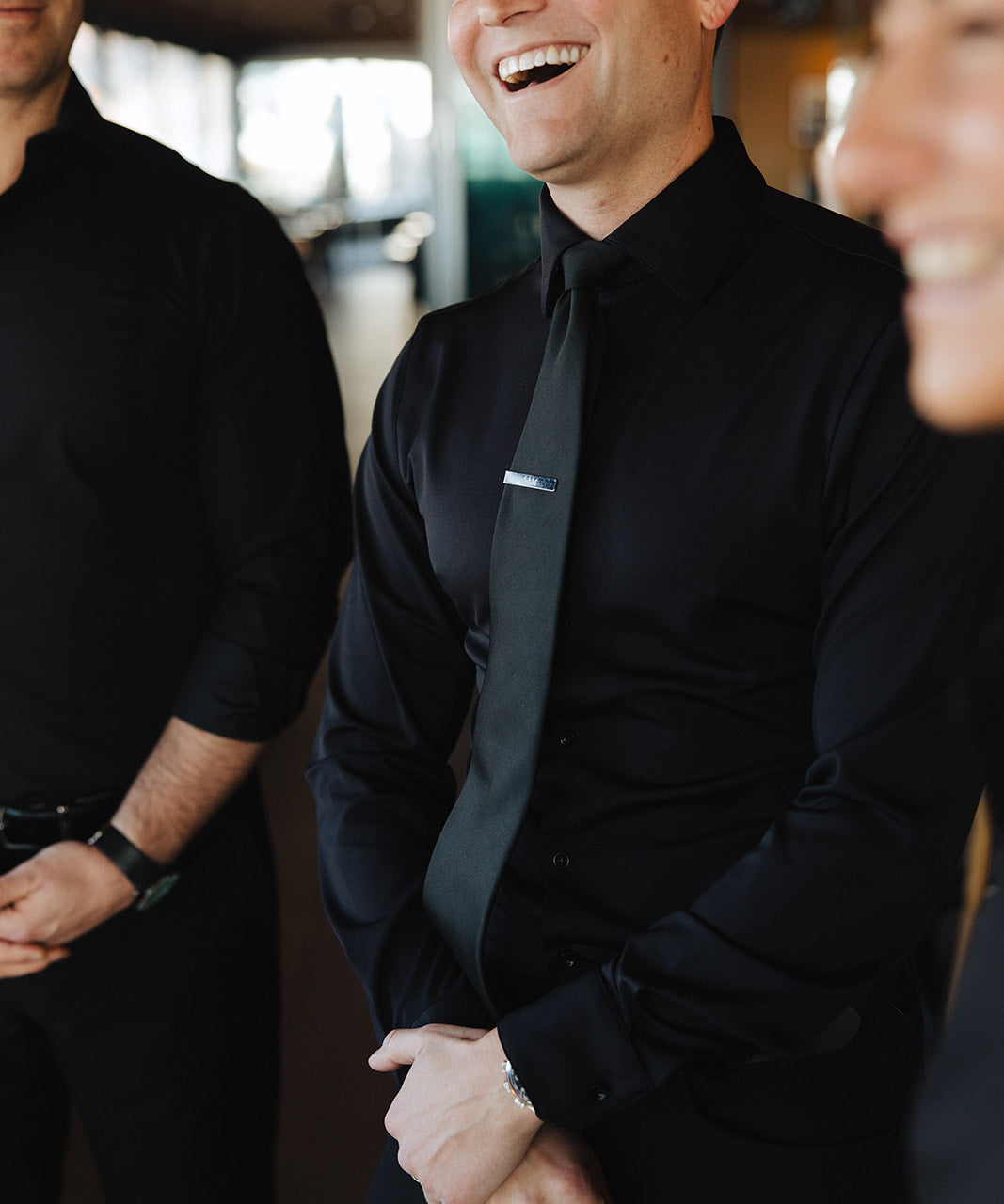 Man wearing black Never-Iron Work Shirt smiling and standing indoors with two other men in black shirts.