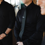 Man wearing black Never-Iron Work Shirt smiling and standing indoors with two other men in black shirts.