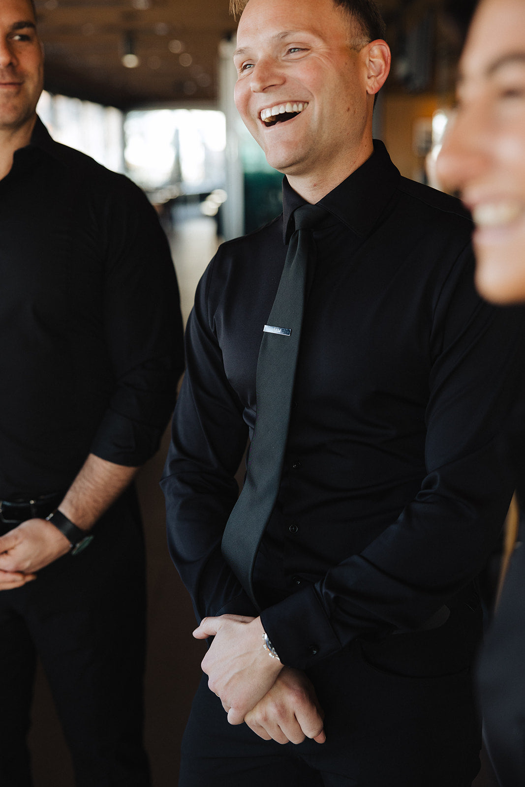 Man wearing black Never-Iron Work Shirt smiling and standing indoors with two other men in black shirts.