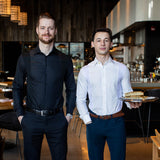 Two men wearing slim fit Men's Work Shirt in black and white, standing in a modern restaurant setting.