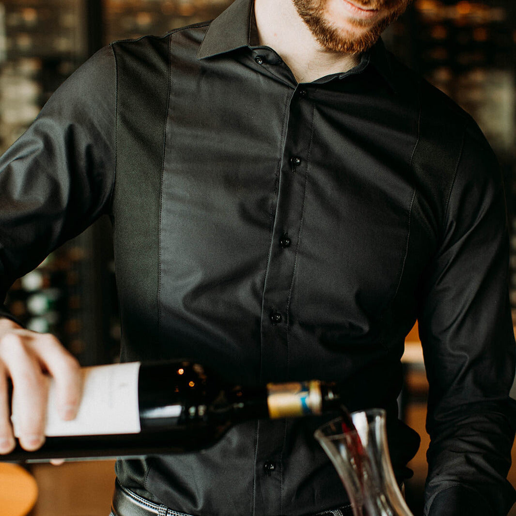 The front of a model wearing a black sweatproof dress shirt for men pouring wine into a decanter