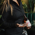 Woman wearing black Women's Work Shirt holding a wine bottle and glass in a stylish setting