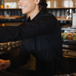 Woman smiling and working behind bar wearing black Women's Work Shirt with seamless fit and wrinkle-resistant fabric