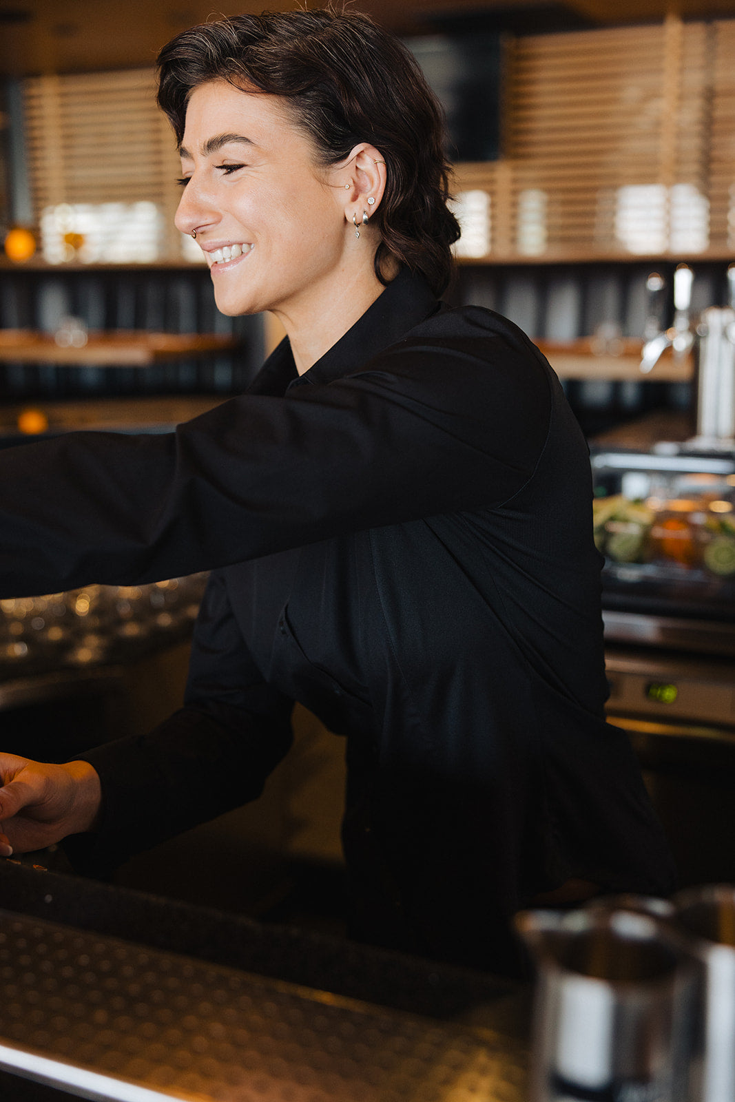 Woman smiling and working behind bar wearing black Women's Work Shirt with seamless fit and wrinkle-resistant fabric