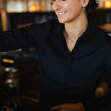 Woman wearing black Women's Work Shirt smiling while working behind a counter in a cozy setting