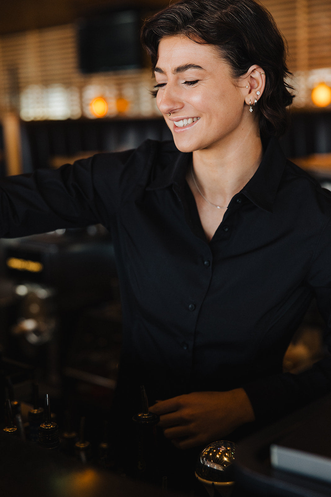 Woman wearing black Women's Work Shirt smiling while working behind a counter in a cozy setting