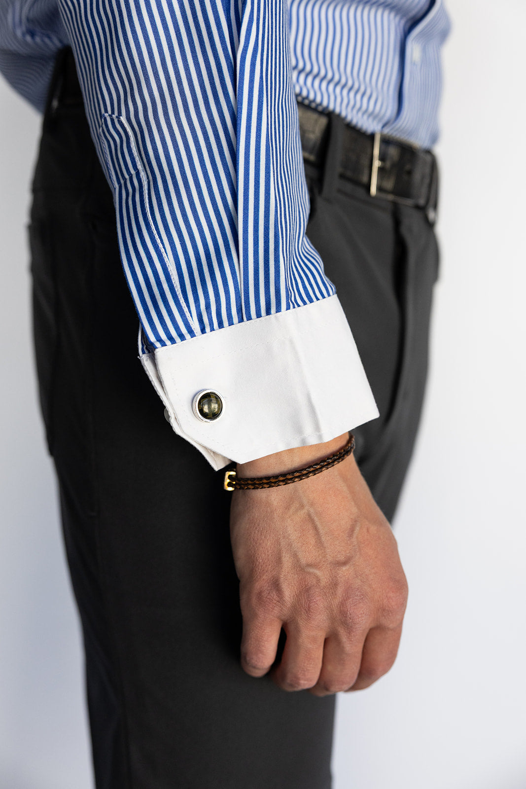 Close-up of a person wearing a blue and white striped shirt with rolled-up sleeves and black pants.