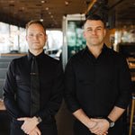 Two men wearing black Never-Iron Work Shirts standing side by side in a stylish indoor setting.