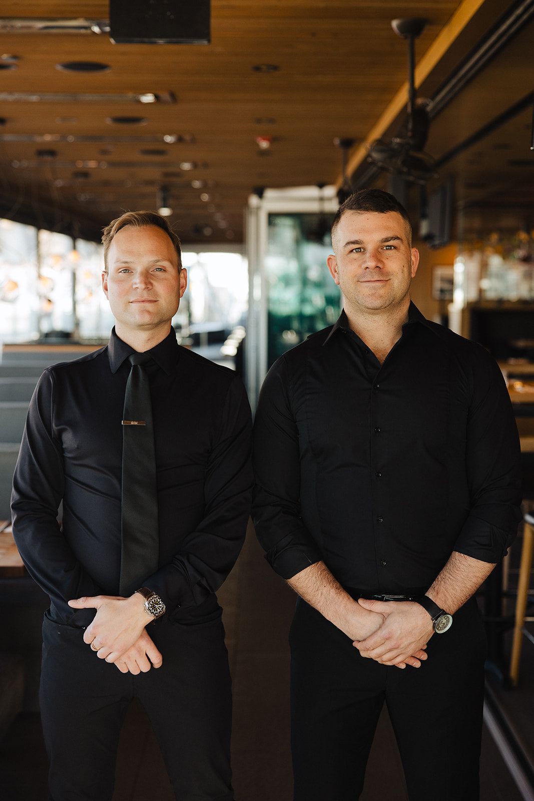 Two men wearing black Never-Iron Work Shirts standing side by side in a stylish indoor setting.