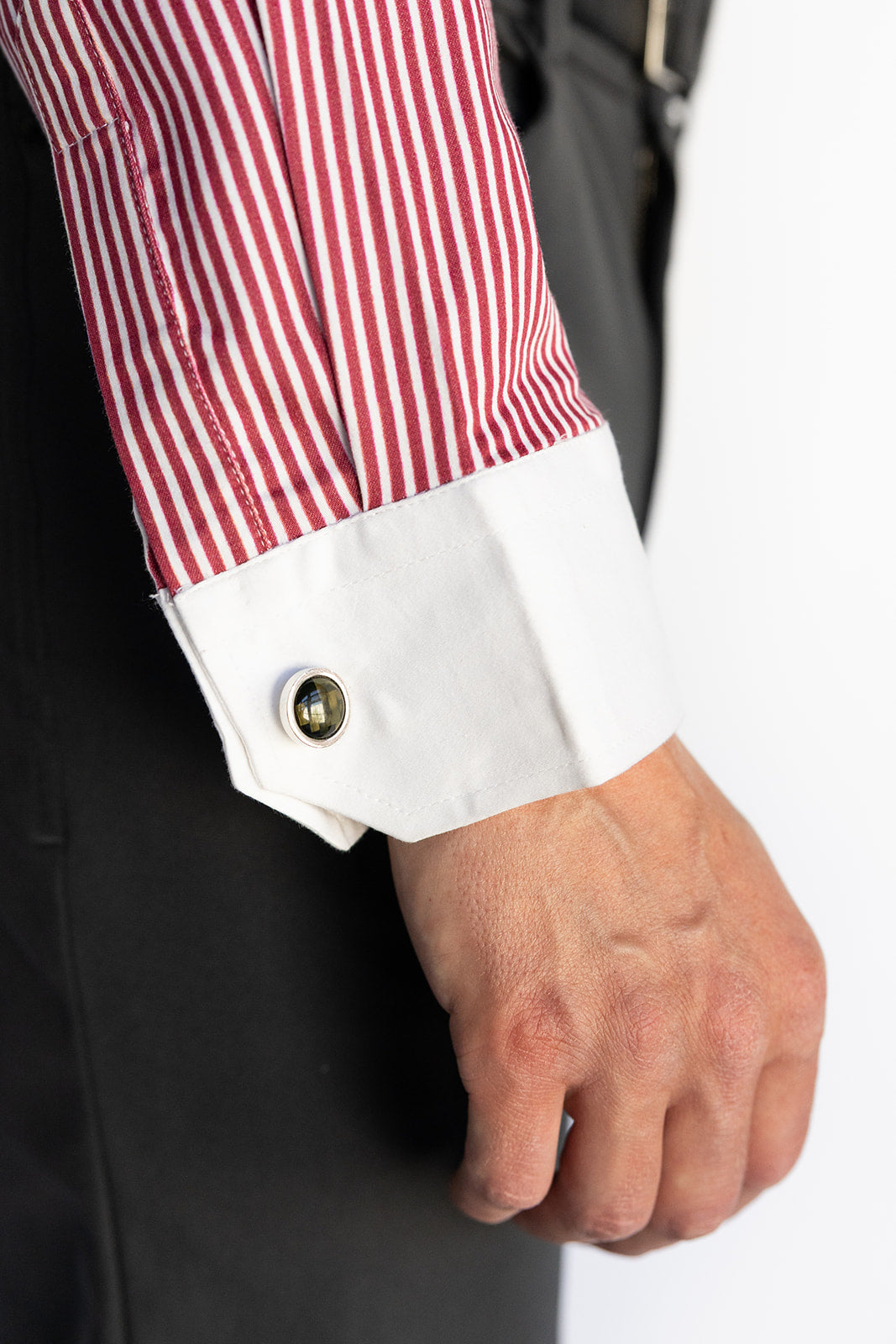 Close-up of a red and white striped shirt cuff with a button, worn with a dark suit.