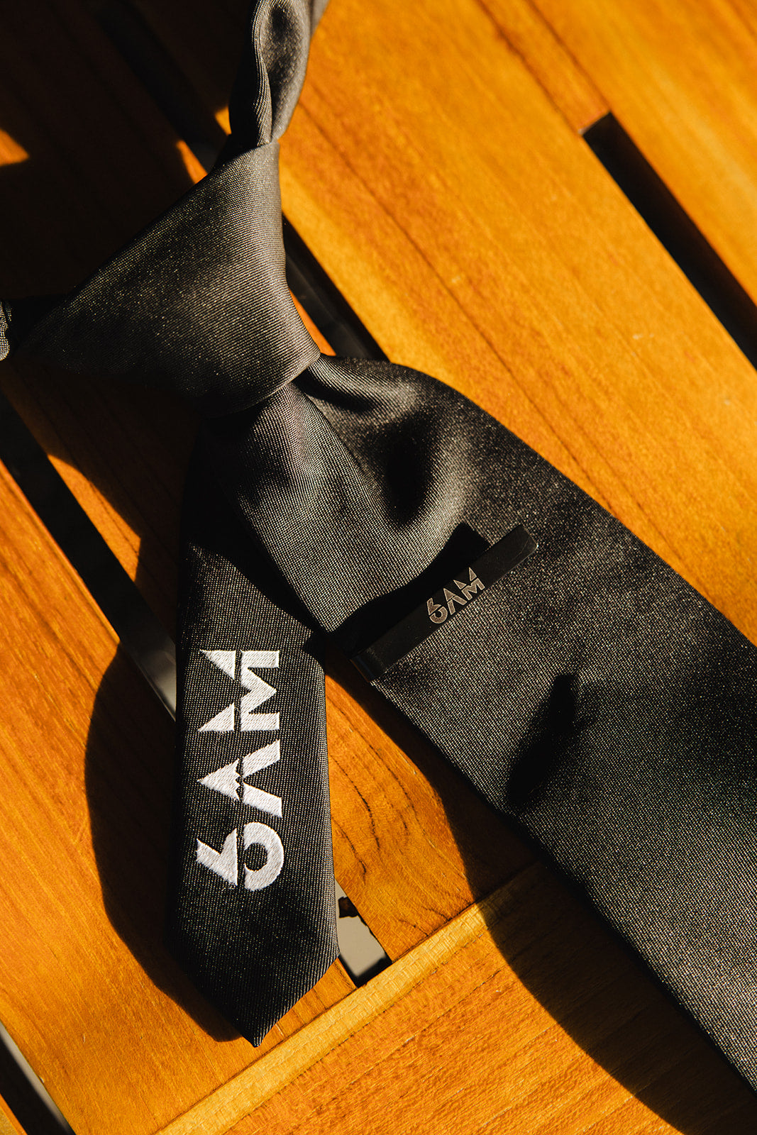 6AM Formal Black Tie close-up on wooden surface featuring black fabric and 6AM logo on the tail.