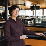 Woman wearing the long-sleeve Bordeaux Arrowhead WorkShirt in a restaurant setting while holding a serving tray.