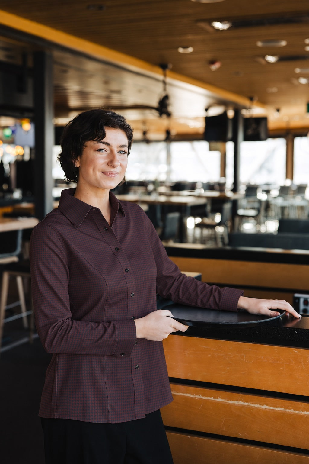 Woman wearing the long-sleeve Bordeaux Arrowhead WorkShirt in a restaurant setting while holding a serving tray.