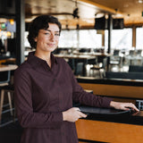 Woman wearing the long-sleeve Bordeaux Arrowhead WorkShirt in a restaurant setting while holding a serving tray.