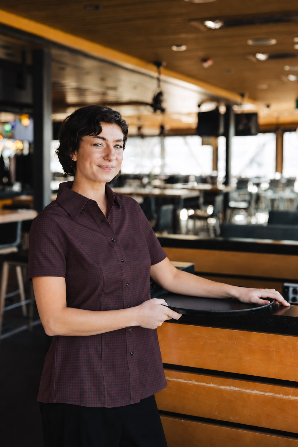Woman wearing the short-sleeve Bordeaux Arrowhead WorkShirt in a restaurant setting while holding a serving tray.