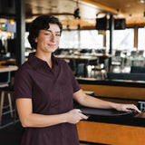 Woman wearing the short-sleeve Bordeaux Arrowhead WorkShirt in a restaurant setting while holding a serving tray.